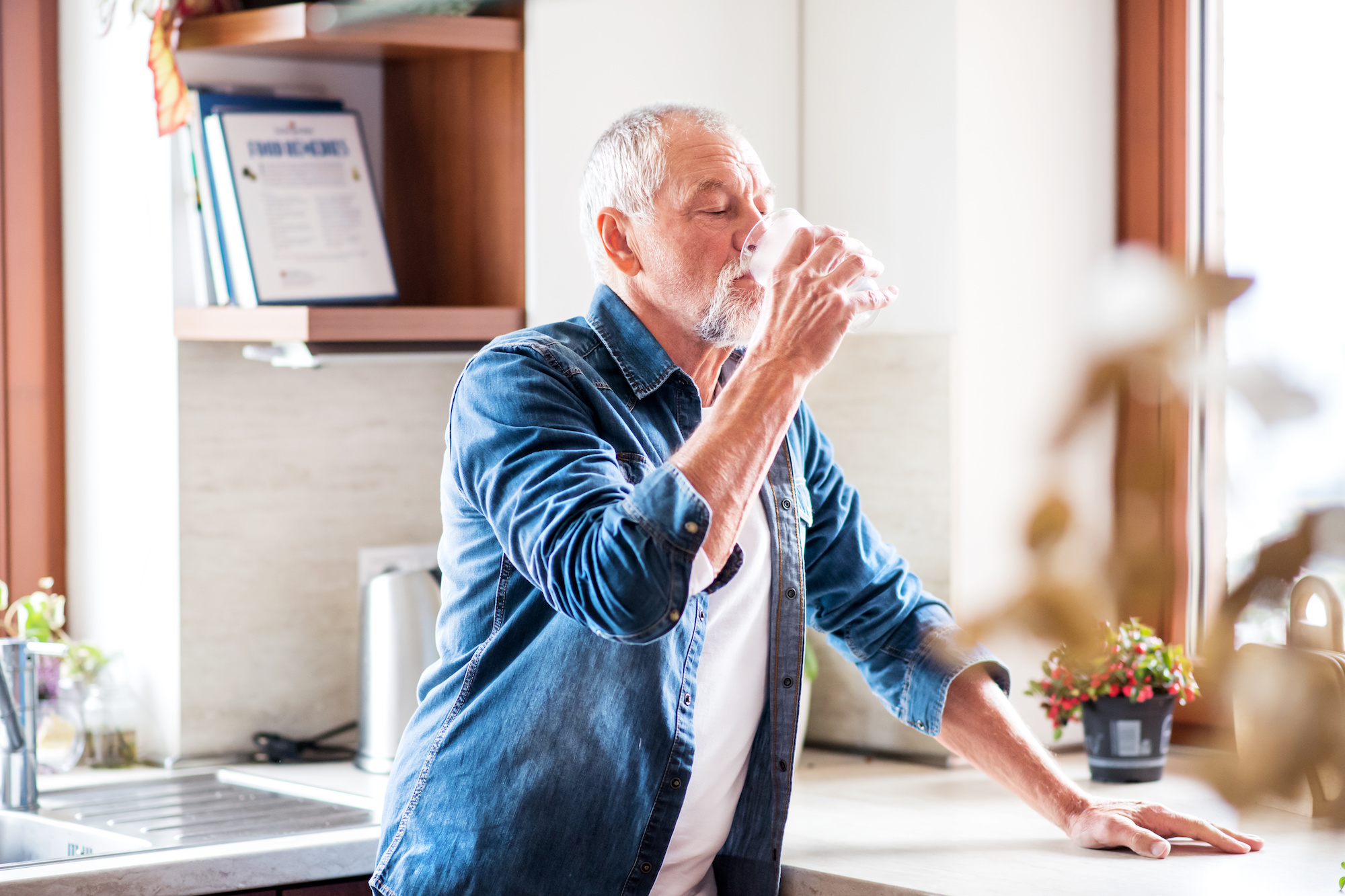 Senior man drinking water in the kitchen to prevent kidney stones | Urology Associates | Denver, CO